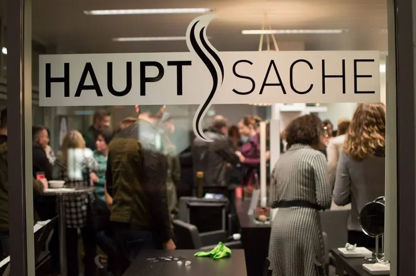 Fenster mit dem Schriftzug HAUPTSACHE und Einblick in den Salon Coiffeur HAUPTSACHE Kriens während einer Veranstaltung mit Gästen