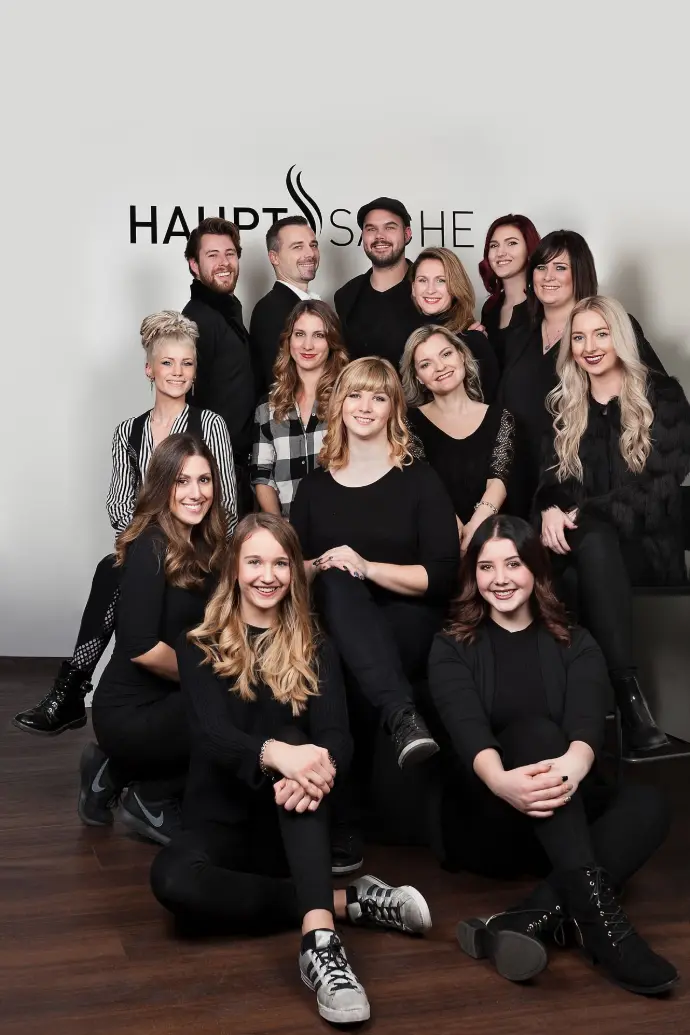 Gruppenfoto des Teams von Coiffeur HAUPTSACHE Kriens vor einer Wand mit dem Salon-Logo